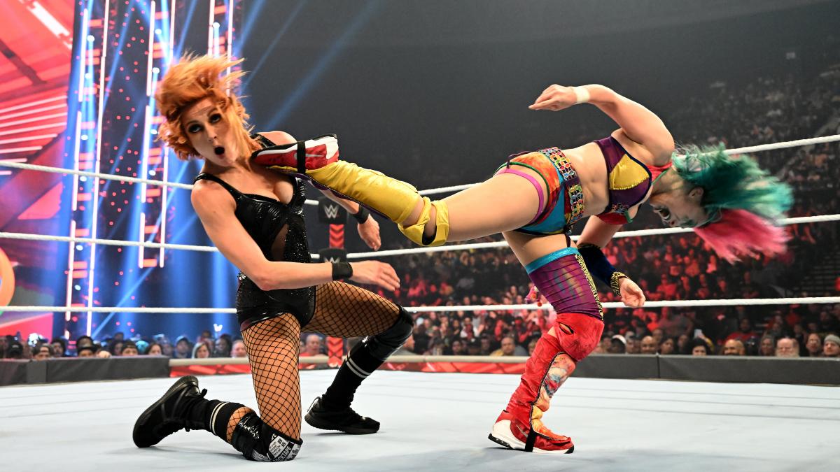 A picture from wrestling event WWE Monday Night Raw. Felmale wrestler Becky Lynch recoils with a stunned expression as she takes a kick to the face from opponent Asuka.